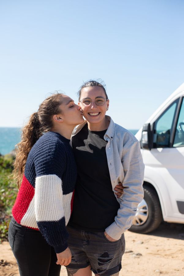 Two women smiling by a van near the sea