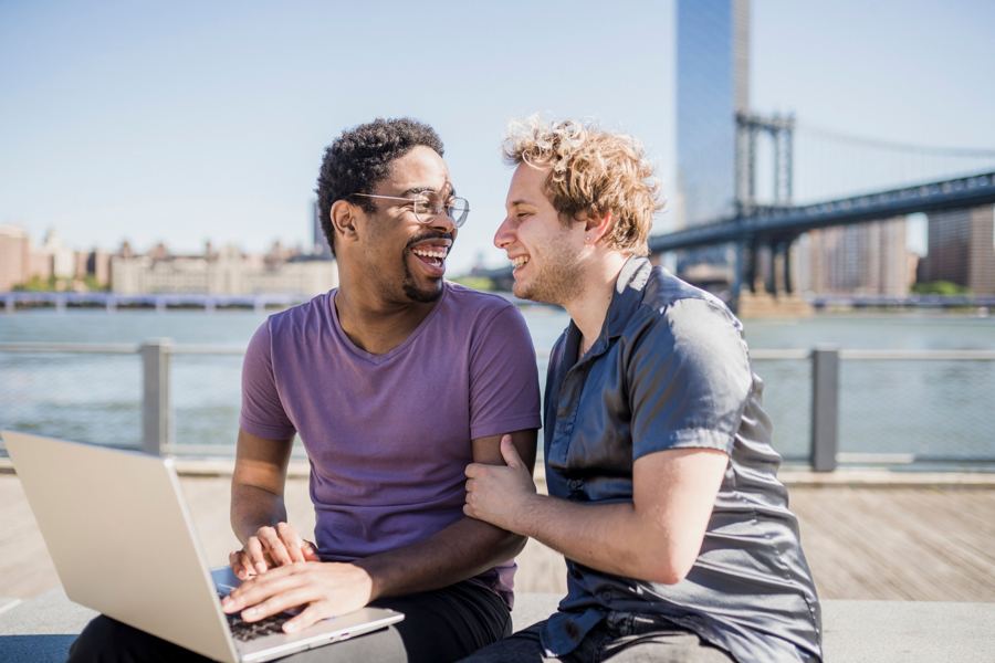 Two friends laughing over a laptop by the river
